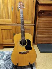 A natural-wood acoustic guitar standing upright in front of wooden furniture.