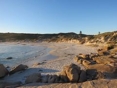 A sandy and rocky coastal cove beside blue water under a clear sky.