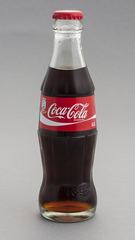 A clear glass beverage bottle containing dark liquid, with a red cap and printed label.