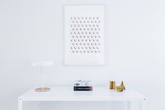 A mostly empty white tabletop with a small lamp, books and small decorative objects.