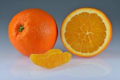 A whole orange, a halved orange and a peeled segment on a gray background.