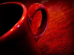 Close-up of a glossy red ceramic mug and its handle on a reddish wooden surface.