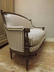 A wooden settee upholstered in narrow light and dark striped fabric.