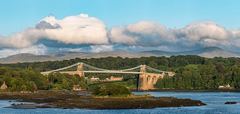A suspension bridge with towers and visible cables crossing water between green banks.