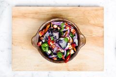 An overhead view of a bowl containing a colorful prepared vegetable salad on a wooden board.